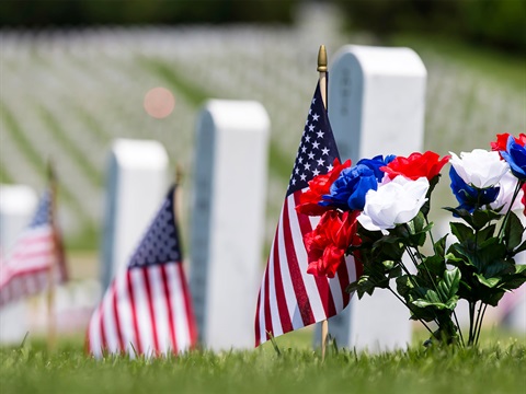 US-Flag-and-red-white-and-blue-flowers-next-to-white-gravestone-at-a-national-cemetery.jpg