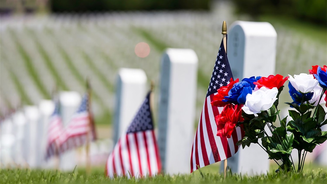 Close-up-of-red-white-and-blue-artificial-flowers-and-American-flags-in-front-of-white-marble-headstones-at-military-veterans-cemetery.jpg