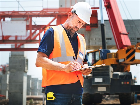 Construction-inspector-holds-clipboard-on-job-site-in-front-of-crane.jpg