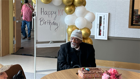 Community member Henry Rainer celebrating his 101st birthday with a cake and balloons at the Senior Center