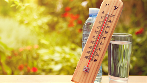 Thermometer on table sitting next to glass of water and plastic water bottle.