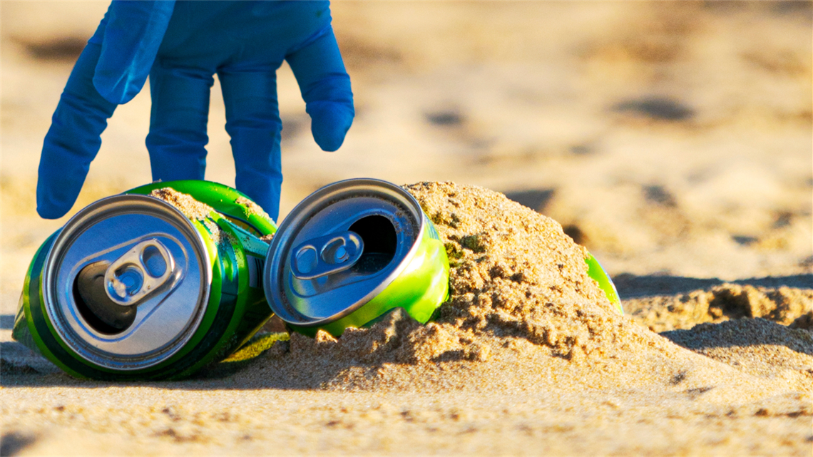 Gloved hand picking up cans on the beach