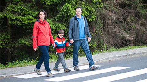 Woman and man and child walking across street while both holding young boy's hands