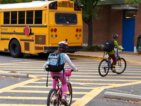 children-ride-bicycle-on-school-property-in-crosswalk-behind-school-bus.jpg