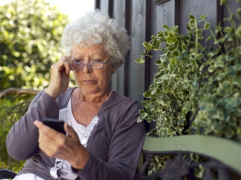 Older-adult-woman-looks-at-her-mobile-phone-while-sitting-outside.jpg