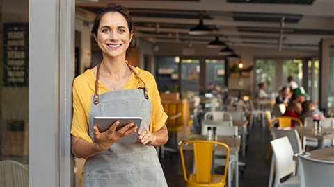 Small-business-restaurant-hostess-smiles-while-holding-a-tablet-and-standing-in-doorway.jpg