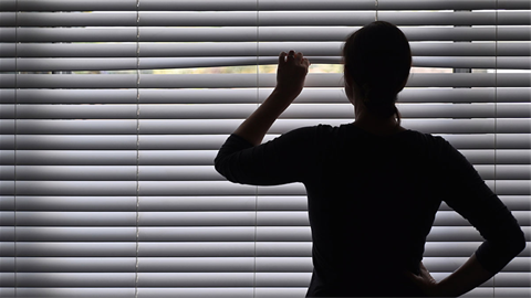 Woman peeking out window blinders in the dark