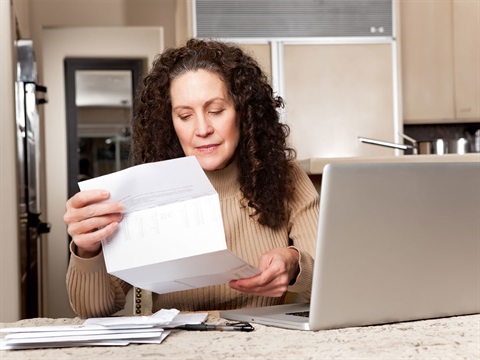 Woman-reviews-her-bills-in-the-kitchen-with-a-laptop.jpg