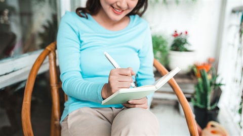 woman-writes-in-a-notebook-while-sitting-on-a-patio (1).jpg