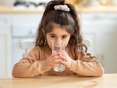 young-girl-drinks-water-from-a-glass-sitting-at-kitchen-table.jpg