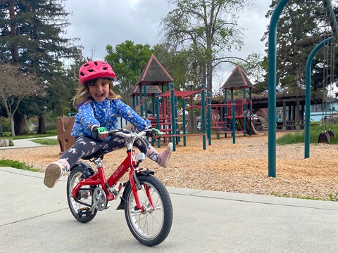 Young-girl-rides-bicycle-on-the-sidewalk-next-to-playground.jpg