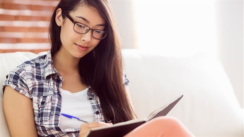 Young-woman-writes-in-a-notebook-while-sitting-on-the-couch.jpg