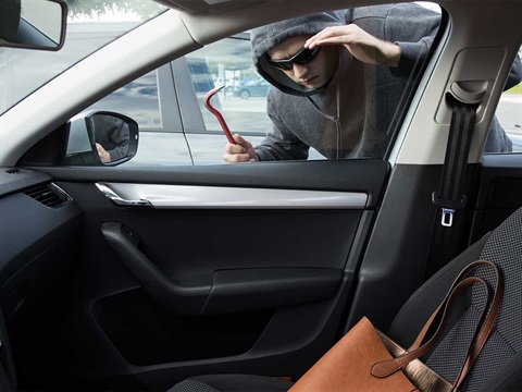 Thief-holding-crow-bar-looks-through-car-window-at-purse-on-seat