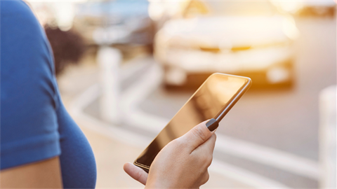 Person holding phone waiting for rideshare with car in distance